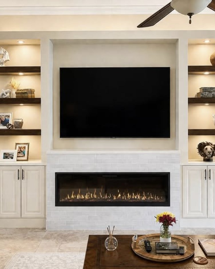 Lit built-in shelving surrounding a linear fireplace and wall-mounted television