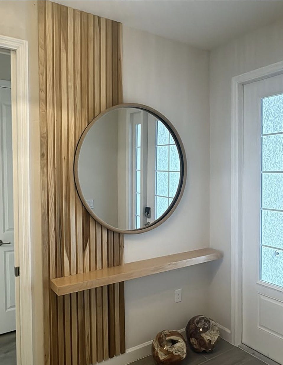Vertical wood slat accent wall with a round mirror and floating shelf in an entryway